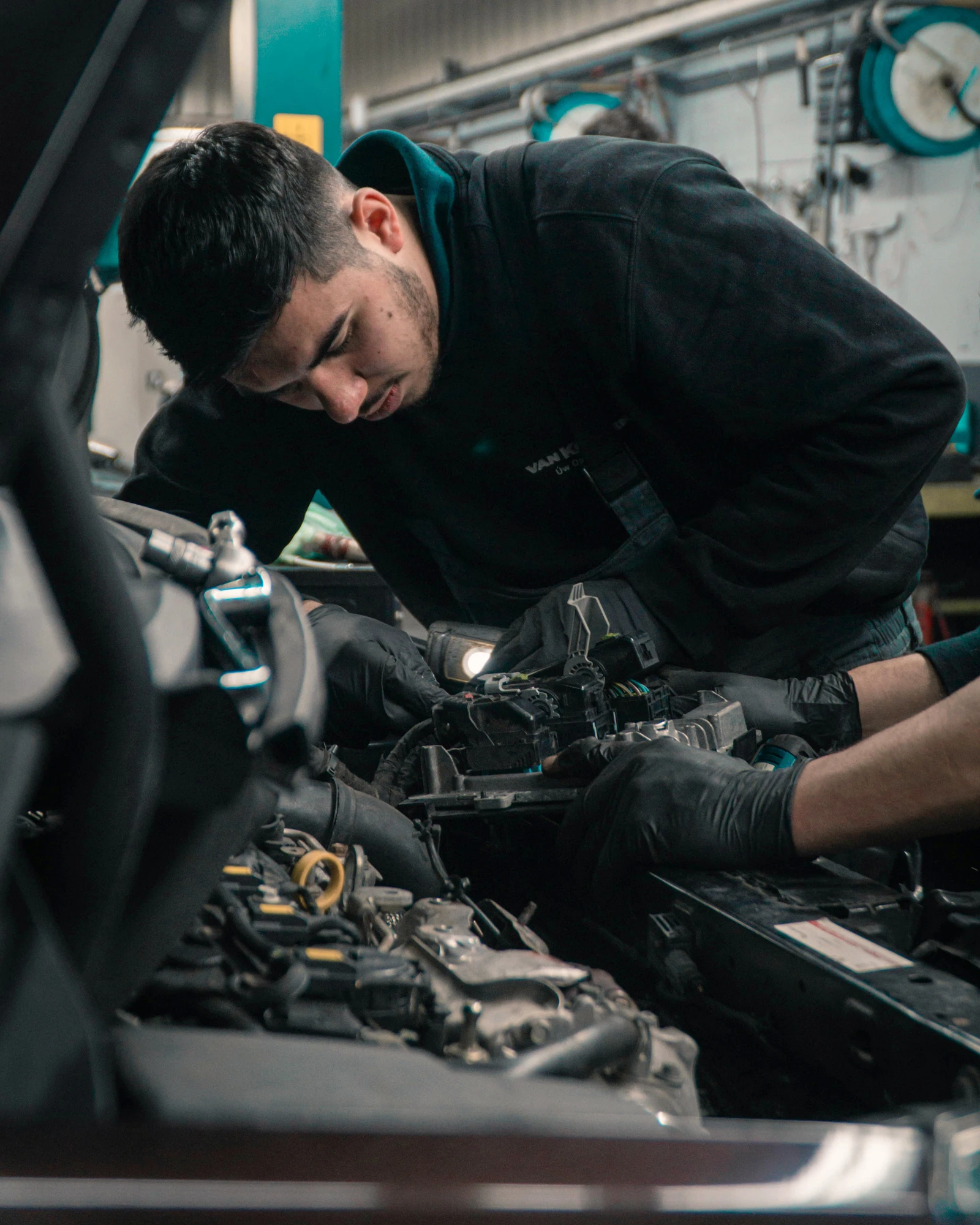 Kfz-Mechatroniker arbeitet im Motorraum eines Autos in der Werkstatt